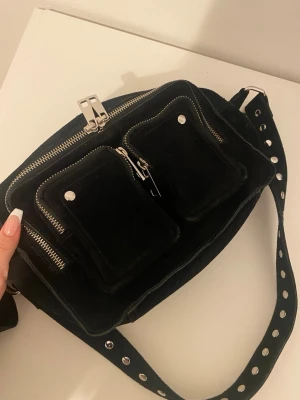 Svart nunoo väska - Jättesnygg äkta svart axelväska i mocka med flera dragkedjefack och silverfärgade detaljer. Använd fåtal gånger men är i perfekt skick! 