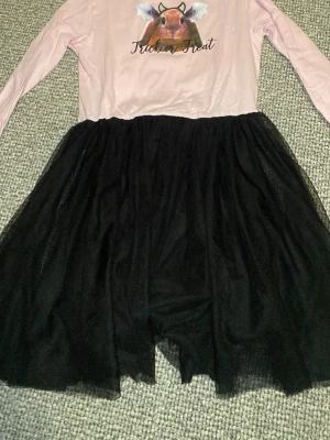 Rosa och svart Halloweenklänning - Säljer en söt klänning med rosa överdel och svart tyllkjol. Överdelen har ett gulligt tryck med en hamster med fladdermusvingar och texten 'Trick or Treat'. Klänningen har långa ärmar och passar perfekt till Halloween eller temafest.
