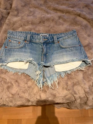Blå jeansshorts från Weekday - Säljer ett par ljusblå jeansshorts från Weekday med råa, fransiga kanter och klassisk femficksdesign. Shortsen har normal passform och low waist, perfekta för sommardagar. Knappt används pga att de är för små! Pris kan diskuteras💕💕