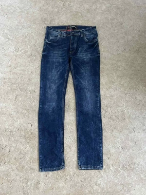 Blå jeans från Polo Ralph Lauren - Snygga blå jeans från Polo Ralph Lauren med klassisk femficksdesign och raka ben. Jeansen har en mörk tvätt med slitningar och kontrastsömmar, samt en läderpatch med logga bak på midjan. Perfekt för dig som gillar en tidlös och cool stil.