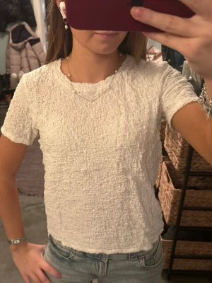 Vit strukturerad topp från Uniqlo - Säljer en vit topp från Uniqlo i storlek M. Toppen har en cool, strukturerad yta och är kortärmad med rund hals. Perfekt att styla med jeans eller kjol för en fräsch look.