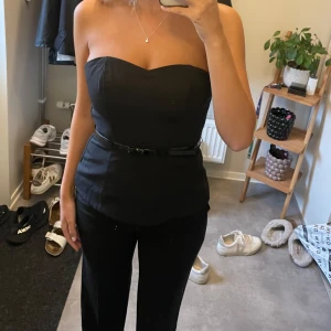 Svart axelbandslös topp med bälte - Säljer en svart axelbandslös topp med smalt bälte i midjan. 