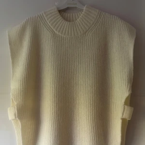 Ny. Stickad vit väst från Gina Tricot - Säljer en chunky stickad väst från Gina Tricot i offwhite. Västen har bred ribbstickning, hög krage och coola slitsar i sidorna med breda band. Perfekt att slänga över en skjorta eller långärmad för en trendig lager-på-lager-look. Storlek M, men den är oversize och kan passa även L.