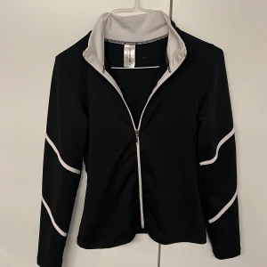 Svart oanvända konståkoing jacka ChloeNoel - Säljer min oanvända konståkoings kofta med vita detaljer. Perfekt för träning på is, fyspass eller bara som ett snyggt lager. Materialet är stretchigt och följsamt. NYPRIS 699kr ⛸️🌟storlek XS-S