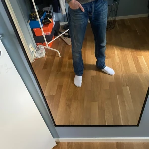 Blå Nudie Jeans, W32 L34 - Säljer ett par klassiska blå jeans från Nudie Jeans med snygga slitningar och kontrastsömmar. Modellen har raka ben, fem fickor och ikonisk broderad detalj på bakfickorna. Perfekta för dig som gillar en tidlös och avslappnad look.
