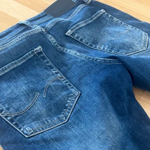 Blå Jack & Jones jeans med raka ben - Snygga blå jeans med klassisk tvätt och raka ben. Jeansen har fem fickor, kontrastsömmar och subtila slitningar för en cool look. Perfekta för dig som gillar en tidlös stil och vill ha ett par jeans som funkar till det mesta.