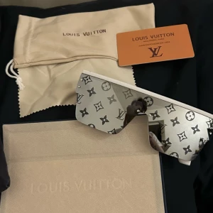 Monogram solglasögon - Säljer ett par sjukt snygga solglasögon med spegelglas och ikoniskt monogrammönster. Glasögonen har en futuristisk, kantig form och vit båge. Perfekt för dig som vill sticka ut med lyxig designerstil.