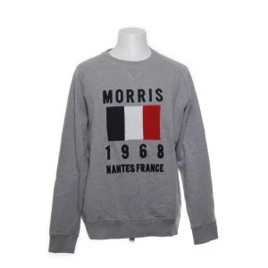 Grå sweatshirt från Morris - Snygg grå sweatshirt från Morris med tryck framtill i form av franska flaggan och texten 'Morris 1968 Nantes France'. Tröjan har rund halsringning och långa ärmar. Perfekt för dig som gillar stilren och sportig look. L men passar M