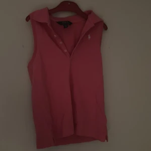 Rosa ärmlös pikétopp Polo Ralph Lauren - Säljer en rosa ärmlös pikétopp från Polo Ralph Lauren med klassisk krage och knappar framtill. Toppen har den ikoniska vita logon broderad på bröstet och är tillverkad i mjuk bomull. Perfekt för en sportig och preppy look. Den finns även inte längre på ralph lauren hemsidan och därför säljer jag den för ett högre pris!