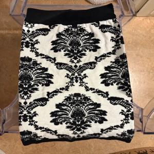 Svartvit mönstrad stickad kjol - Säljer en svartvit stickad kjol med ett snyggt, barockinspirerat mönster. Kjolen har bred svart midjeresår och är i kort modell. Perfekt för dig som gillar unika plagg med coola detaljer.