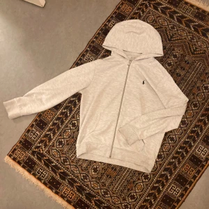 Grå kofta från Polo Ralph Lauren - Snygg ljusgrå hoodie från Polo Ralph Lauren med dragkedja framtill och klassisk broderad logga på bröstet. Ja fraktar inom 24 timmar✅ pris kan diskuteras. Skriv om du har frågor