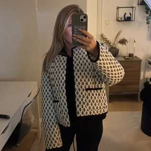 Höst jacka - Quiltad overshirt i vit med svart mönster och svarta kantdetaljer. Jackan har rund hals, två fickor framtill och långa ärmar. Mönstret är droppformat och ger en cool, unik vibe. Perfekt för lager-på-lager och att styla med jeans eller kjol. Aldrig använd❤️sitter som xs