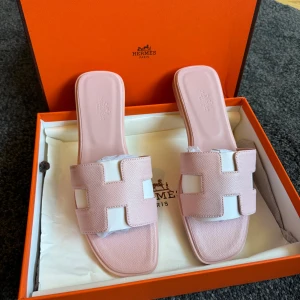 Rosa H sandaler  - Säljer ett par lyxiga H sandaler i ljusrosa skinn med den ikoniska H-detaljen framtill. De har fyrkantig tå och platt sula, perfekt för en stilren och trendig look. Kommer i originalask. Superfina att matcha med sommarens outfits!