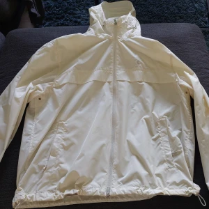 Vit vindjacka från Polo Ralph Lauren - Snygg vit vindjacka från Polo Ralph Lauren med huva och dragkedja framtill. Jackan har två fickor med lock, justerbar nederkant och diskret logga på bröstet. Perfekt för blåsiga dagar och enkel att matcha med allt. 