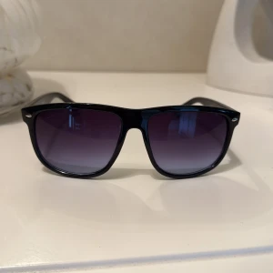 Svarta solglasögon med lila ton - Snygga solglasögon med svart, glansig båge och rektangulär form. Glasen har en cool lila toning som ger en modern vibe. Passar perfekt för soliga dagar och har UV400-skydd. Stilren design som funkar till de flesta.