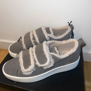 Grå sneakers med teddyfoder från Duffy - Mysiga grå sneakers från Duffy med fluffigt teddyfoder och breda kardborreband. Populära och slutsålda, helt nya