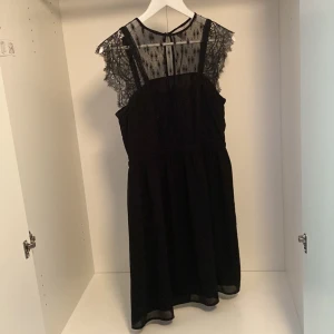 Svart spetsklänning från H&M - Supersnygg svart klänning från H&M med transparent spets upptill och fina spetsärmar. Klänningen har ett diskret mönster i spetsen och en rund halsringning med knapp i nacken. Kjolen är lätt utställd och längden är ovanför knäet. Perfekt för dig som gillar detaljer och stilren look.