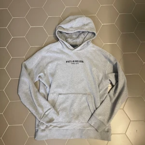 Grå hoodie från Paul & Shark - Ljusgrå hoodie från Paul & Shark med broderad logga på bröstet. Tröjan har huva, magficka och är tillverkad i mjuk fleece, perfekt för kyliga dagar. Klassisk passform och långa ärmar gör den både stilren och bekväm.