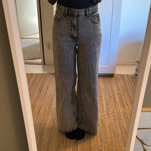Gråa wide jeans med hög midja - Säljer ett par gråa jeans med snygg tvätt, hög midja och breda ben. Klassisk femficksmodell med bälteshällor och dragkedja. Perfekta för dig som gillar en avslappnad och trendig stil.