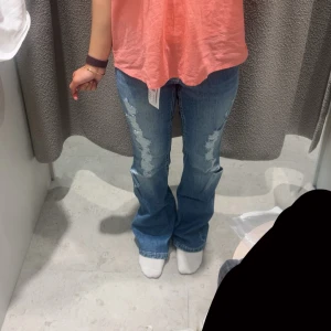 Blå bootcut jeans med slitningar - Säljer ett par blå bootcut jeans med snygga slitningar framtill. Jeansen har klassisk femficksmodell och justerbar midja på insidan. Använd några gånger, men det finns lite slitage och smuts på benen, vilket förmodligen kommer att försvinna med en enkel tvätt. Så jag har inte försökt tvätta smutsen. Fråga förstås om något dyker upp. 💕
