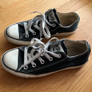 Svarta Converse All Star sneakers - Klassiska svarta låga Converse All Star sneakers med vit tå och vita snören. Lågt skaft, rund tå och platt sula. Skorna är i canvas med tydliga kontrastsömmar och gummidetaljer. 
