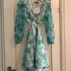 Blommig cut out klänning från SHEIN - Superfin kort klänning från SHEIN med blågröna blommor, v-ringning och långa puffärmar. Klänningen har snygga cut outs i midjan och är gjord i ett lätt, transparent polyestertyg med innerfoder. 