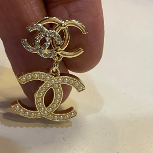  örhängen med pärlor och strass - Statementörhängen  i guldtonad metall med dubbla . Den övre loggan är dekorerad med glittrande strass och den nedre med små vita pärlor. Perfekta för dig som vill sticka ut och addera lyx till din look.