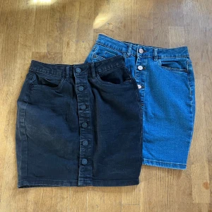 Två jeanskjolar från Noisy May XS - Säljer två snygga jeanskjolar från Noisy May i storlek XS. En är svart och en är klassiskt blå, båda med knappar framtill och fickor. Modellen är rak och kort, perfekt till sneakers eller boots. Materialet är jeans med en skön passform.