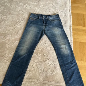 Blå jeans från Diesel - Snygga blå jeans från Diesel med klassisk femficksdesign och diskret slitning på låren. Jeansen har raka ben och normal passform, tillverkade i slitstarkt denim. Perfekta för dig som gillar en tidlös och avslappnad stil.