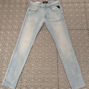 Replay Anbass Hyperflex ljusblå jeans - Säljer ett par Replay Anbass Hyperflex jeans i ljusblå tvätt. Jeansen har klassisk femficksdesign, raka ben och normal passform. Materialet är stretchigt för extra komfort och rörelsefrihet. Perfekta för dig som gillar en clean och stilren look.