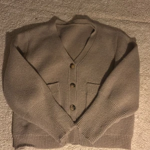 Beige stickad kofta med knappar - Mysig beige stickad kofta med v-ringning och tre bruna knappar framtill. Koftan har två fickor på framsidan och ribbade muddar vid ärmslut och nederkant. Perfekt för lager-på-lager och chill höst- eller vinterstil. Så fin till både jeans och mjukis! Pris kan diskuteras!🩷