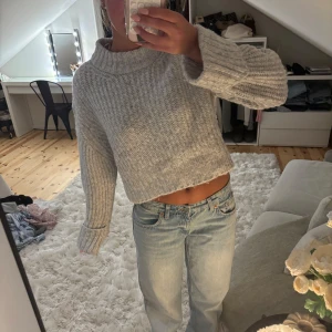 Ljusgrå polo stickad tröja - Supermysig ljusgrå stickad tröja med croppad passform och bred polokrage. Tröjan har grov ribbstickning och långa ärmar, perfekt för lager på lager under kyliga dagar.