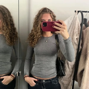 Grå tight långärmad tröja H&M - Slimmad grå långärmad tröja från H&M i mjukt material. Snygg och enkel modell med rund halsringning och ribbade muddar. Perfekt att styla med jeans eller kjol för en clean look.