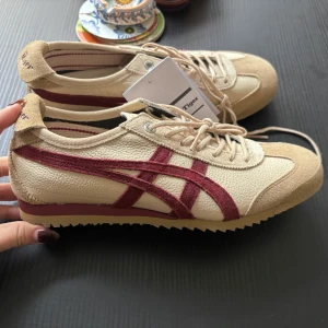 Onitsuka Tiger sneakers  - Snygga Onitsuka Tiger sneakers MEXICO 66 SD i beige med vinröda ränder på sidorna. Skorna har snörning, platt sula och är tillverkade i en mix av skinn och mocka. Helt nya med prislapp! Org pris: 2 400 kr 
