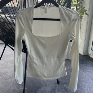 Vit långärmad topp med fyrkantig ringning H&M - Säljer en stilren vit långärmad topp från H&M i storlek XS. Toppen har en snygg fyrkantig ringning och är figurnära i modellen. Tillverkad i mjukt och stretchigt material som känns skönt mot huden. Perfekt att styla med jeans eller kjol för en clean look. Har dock små nopprar på sig