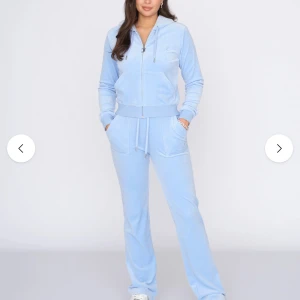 Ljusblå set från Juicy Couture (kofta+byxor) - Supermjuk ljusblå hoodie från Juicy Couture i velour med dragkedja, huva och broderad JC-logga på bröstet. Tröjan har känguruficka och ribbade muddar. Perfekt för chill dagar eller när du vill vara extra comfy.