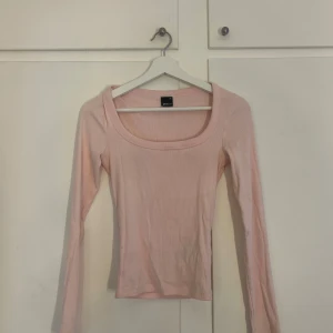 Ljusrosa ribbad långärmad topp Gina Tricot - Ljusrosa långärmad topp från Gina Tricot med ribbad struktur och fyrkantig ringning. Toppen är figurnära och har en enkel, stilren design som passar perfekt till jeans eller kjol.