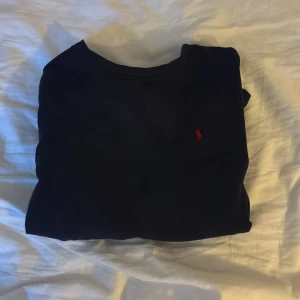 Mörkblå tröja från Polo Ralph Lauren - Klassisk mörkblå tröja från Polo Ralph Lauren med röd broderad logga på bröstet. Tröjan har rund halsringning och långa ärmar, perfekt för en stilren och enkel look. Tillverkad i mjuk bomull som känns skön mot huden.