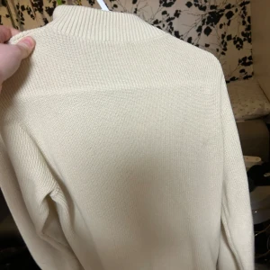 Beige stickad tröja med half zip Kappahl - Beige stickad tröja från Kappahl i storlek 134/140. Tröjan har en ribbad krage och en snygg half zip-dragkedja framtill. Långärmad och i mjukt material som passar perfekt till kyligare dagar.
