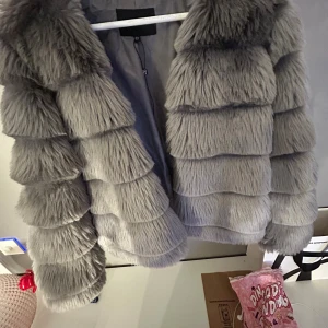 Grå pälsjacka från Parisian - Säljer en fluffig och trendig grå pälsjacka från Parisian i storlek 36. Jackan har långa ärmar och är sydd i breda, horisontella sektioner som ger en cool och lyxig look. Perfekt för dig som vill sticka ut och hålla dig varm med stil. ASS snygg till hösten.