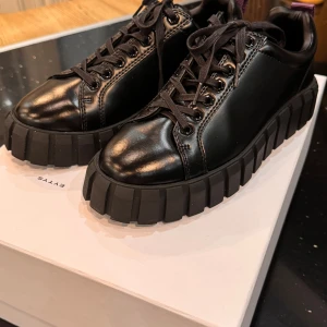 Chunky svarta sneakers från Eytys - Säljer ett par svarta sneakers från Eytys med riktigt chunky sula och coola detaljer. Skorna är i skinn med snörning och har en robust, platt sula som ger en edgy vibe. Perfekta för dig som vill sticka ut med din stil.