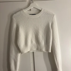 Vit stickad croppad tröja - Superfin vit stickad tröja från FB Sister. Modellen är croppad med bred ribbad mudd i nederkant och vid ärmslut. Mjuk och skön, perfekt till höst och vinter. Rund halsringning och långärmad för en clean och stilren look.