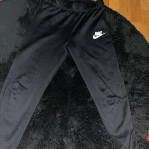 Svarta mjukisbyxor från Nike XL - Svarta mjukisbyxor från Nike i storlek XL med klassisk vit Nike-logga på låret. Byxorna har elastisk midja och är tillverkade i ett mjukt och bekvämt material, perfekta för chill eller träning. Standard fit som ger en avslappnad känsla. Dom passar mer xs/s än XL. Ny pris runt 500 kr.
