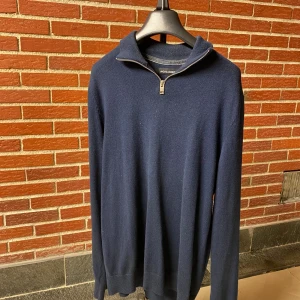 Mörkblå half zip tröja Jack & Jones - Mörkblå stickad tröja från Jack & Jones med half zip-dragkedja i halsen. Tröjan har lång ärm och en klassisk, stilren look som passar perfekt till lager-på-lager. Mjuk och skön, perfekt för kyligare dagar.