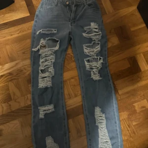 Ljusblå ripped straight jeans - Säljer ett par ljusblå jeans med rejält slitna och trasiga detaljer framtill och på sidorna. Byxorna har rak passform och hög midja, tillverkade i klassiskt jeanstyg. Perfekta för dig som gillar en edgy och trendig streetstil.