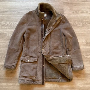 Brunello Cucinelli jacka - Snygg brun skinnjacka från Brunello Cucinelli med mjukt pälsfoder på insidan. Jackan har hög krage, stora fickor med lock och stängs med både dragkedja och tryckknappar. Perfekt för kalla dagar och ger en cool vintagekänsla.