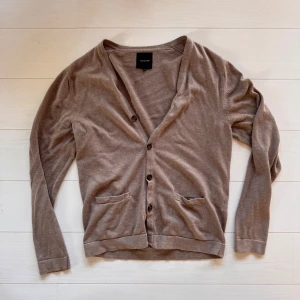 Beige kofta, storlek L - Snygg beige kofta. Klassisk modell med v-ringning, knappar framtill och två fickor. Perfekt att slänga över en t-shirt eller skjorta. Långärmad och enkel att matcha till det mesta.