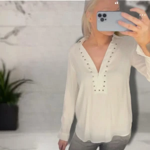 Vit henley-skjorta med nitar - Vit henley-skjorta med långa ärmar och coola silverfärgade nitar längs v-ringningen och axlarna. Skjortan har en avslappnad passform och är tillverkad i ett lätt, mjukt tyg som känns skönt mot huden. Bredd 39 cm, Längd 70 cm