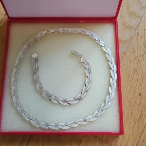 Flätat halsband och armband i silver - Snyggt set med halsband och armband från Guldfynd i flätad design. Båda är i silver 925l med glittrig yta som fångar ljuset. Perfekt för dig som gillar stilrena och trendiga smycken med lite extra detalj. Kommer i original ask.