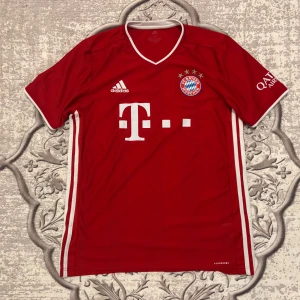 FC Bayern München Adidas matchtröja M - Röd FC Bayern München fotbollströja från Adidas med vita detaljer och klubbmärke på bröstet. Klassisk V-ringning, korta ärmar och AEROREADY-material som andas. Tysklands mästarlag, tryck på ryggen och sponsordetaljer på ärmen.